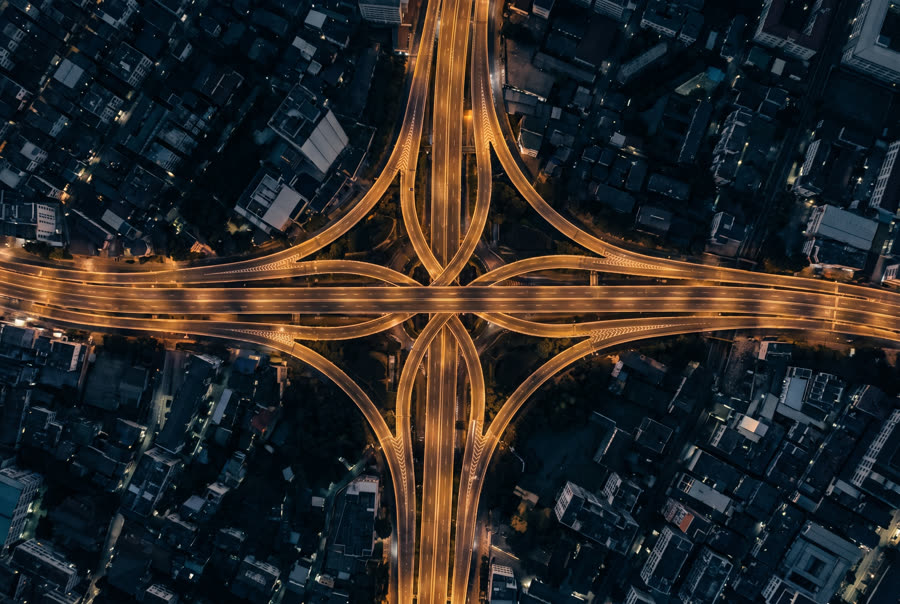 A multi-level expressway interchange at night from directly above, ramps looping as ribbons of warm light
