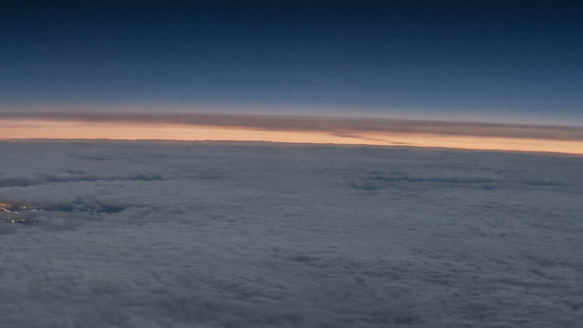 A sea of cloud at first light, with a thin band of dawn along the horizon, seen from high altitude.