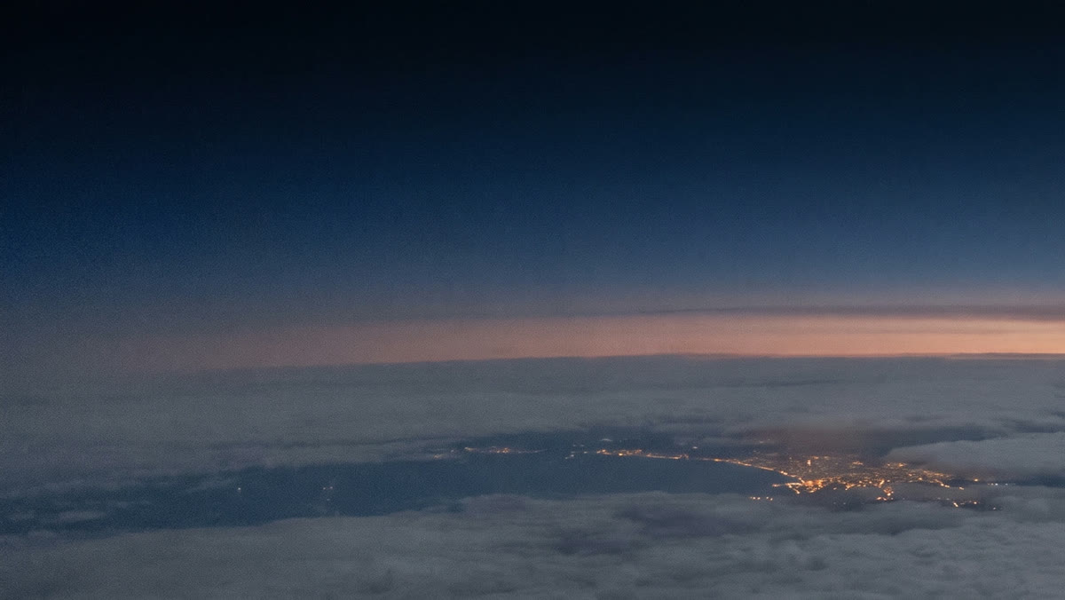 A coastline with city lights under a dark sky just before sunrise, seen from high altitude.