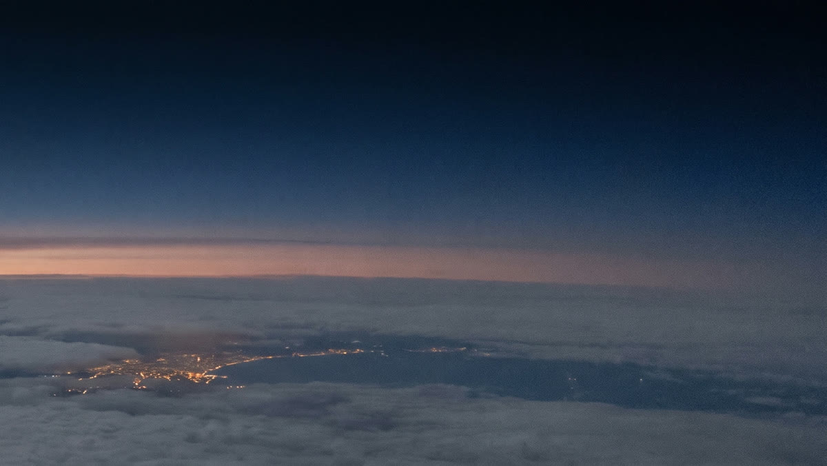 A coastline with city lights under a dark sky just before sunrise, seen from high altitude.