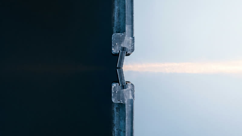 A canal lock seen from directly above, with dark water on one side of the gates and pale water on the other.