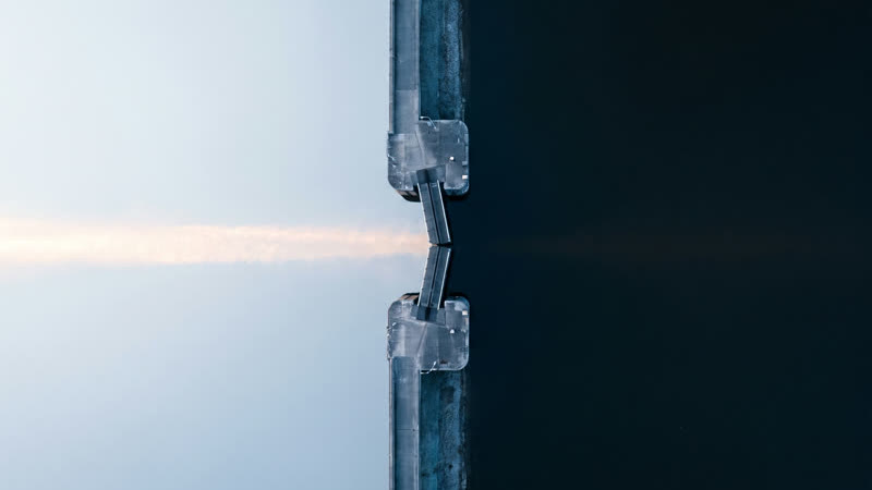A canal lock seen from directly above, with dark water on one side of the gates and pale water on the other.