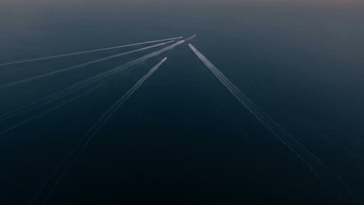 The wakes of several ships converging on dark water, seen from above.