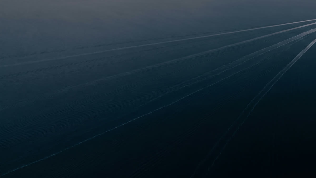 Long, straight ship wakes crossing dark water, seen from above.